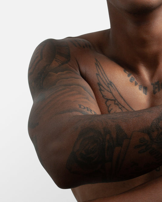 Close-up of a man's muscular arm with visible tattoos, flexing to showcase strength and muscle definition.  This image relates to the U-Pump Black Rhino performance enhancer and its potential to improve strength gains.