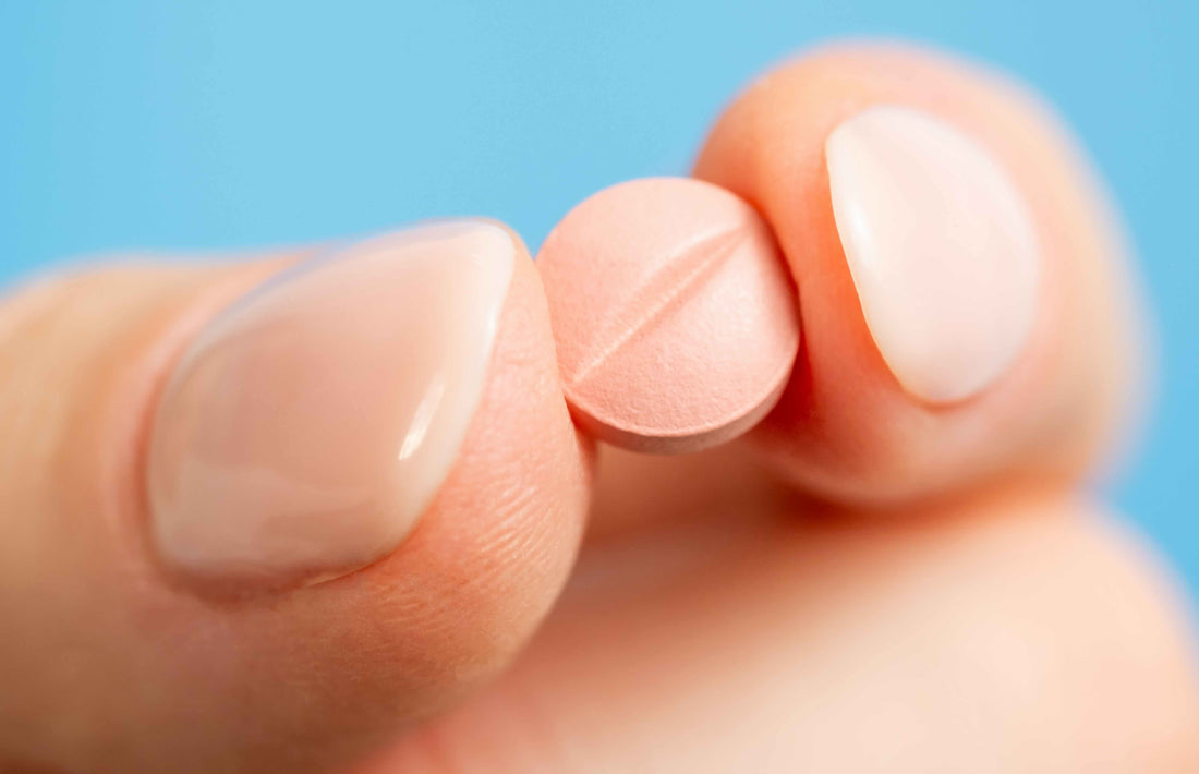 A photo of fingers with healthy nails holding a natural supplement pill.